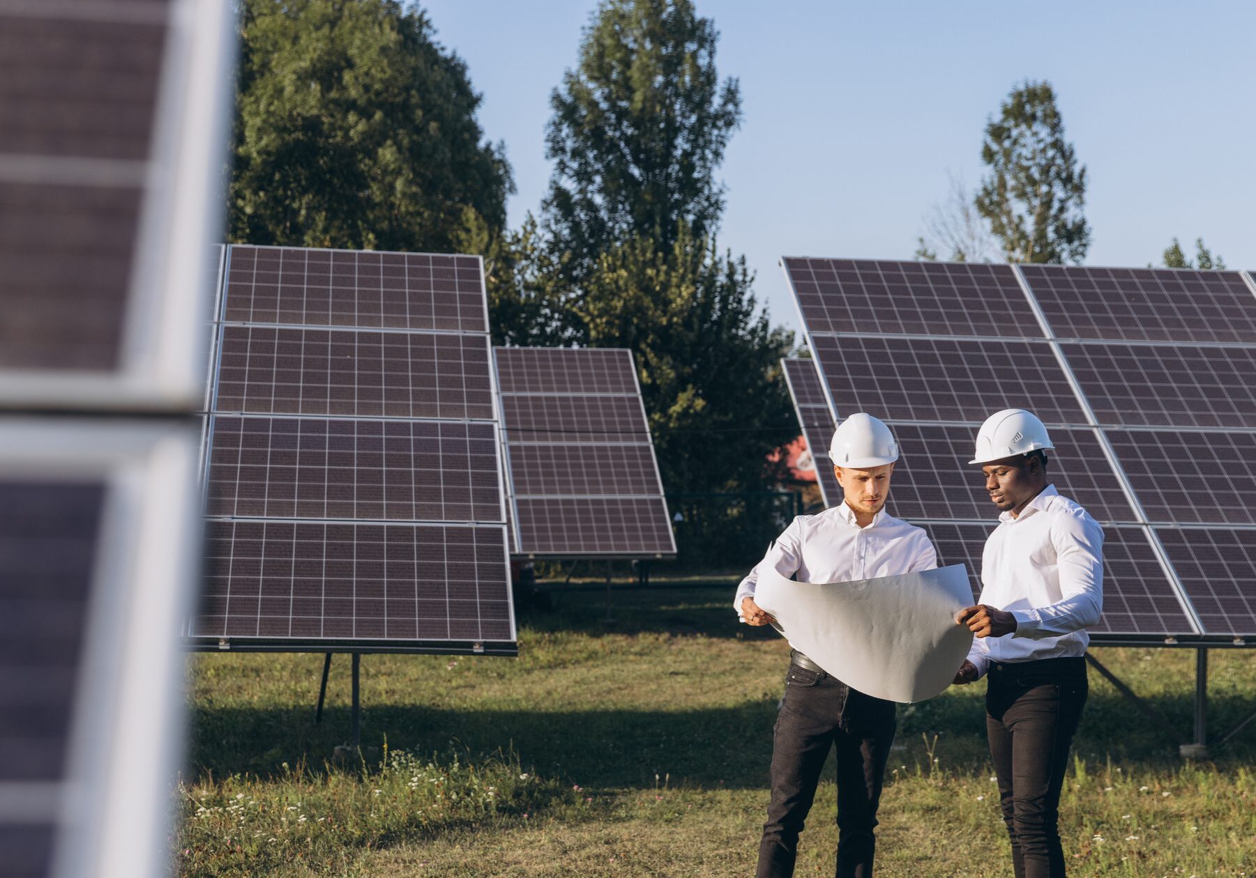 Two engineers at a solar farm examining blueprints, symbolizing teamwork and renewable energy advancements.